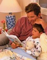 Picture of father listening to his son read a book at bedtime
