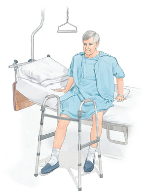 Man in hospital gown sitting on the edge of a hospital bed with his feet flat on the floor. His hands pushing down on the bed on both sides of the body.