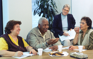 Four people sitting at conference room table, talking.