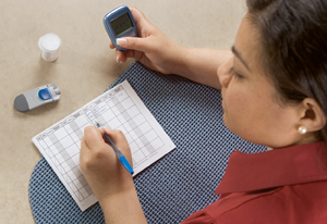 Woman holding glucometer and writing in blood glucose log.