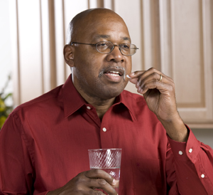 Man putting pill in his mouth while holding glass of water.