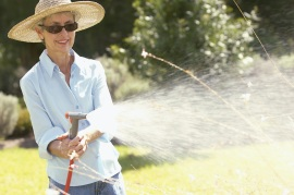 Older woman wearing wide-brimmed hat and long sleeve shirt while watering in the yard