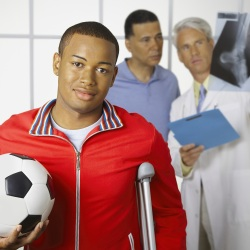 Teen carrying a soccer ball and resting on a crutch at doctor's office