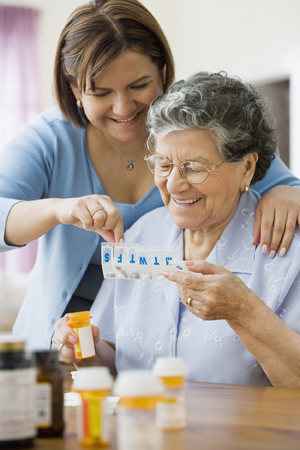 Woman helping senior woman with medication organizer.