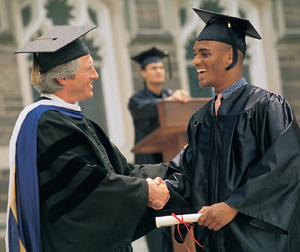 Man wearing cap and gown receiving diploma, graduating from college.