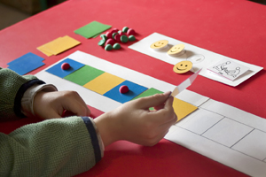 Child placing colored squares in sequence on table.
