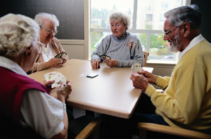 Four seniors playing cards at table.