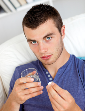 Young man taking pills with glass of water.