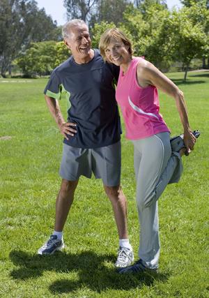 Mature couple exercising in park, woman stretching.