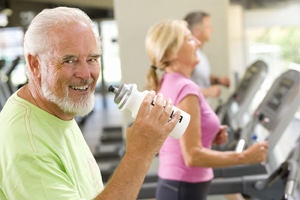 Senior man with water bottle on treadmill, smiling.