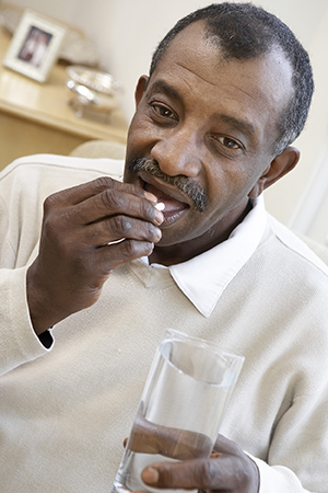 Close up of senior man taking a pill with a glass of water.