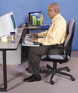 Mature man sitting at desk infront of computer in correct ergonomic position.