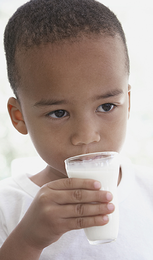 Young boy drinking small glass of milk.