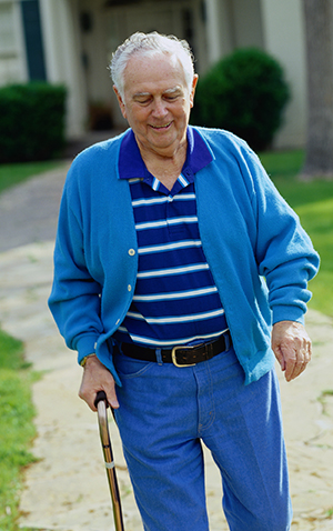 Elderly man walking with cane outside his front door.