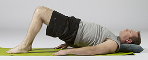 Man lying on floor with knees bent and feet flat on floor, hips raised off floor.