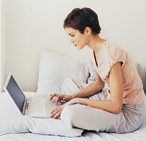 Young woman sitting on bed using laptop computer.
