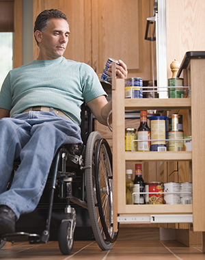 Man in wheelchair in kitchen at accessible food drawer cabinet.