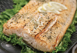 Seasoned salmon on a plate with lemon wedges on a bed of lettuce.