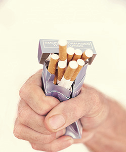 View of man's hand squeezing and crushing a pack of cigarettes