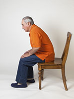 Man sitting at front edge of chair preparing to stand up.