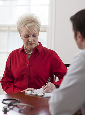 Woman meeting with a doctor. She is writing information on a pad of paper.