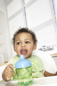 Toddler in a high chair reaching for a sippy cup.