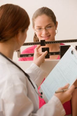 Teen girl having weight checked by health care provider.
