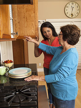 Woman getting dishes from cupboard with younger woman helping.