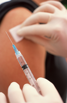 Close up of hands and the upper arm of a woman. One hand is cleaning the injection area, and the other is holding a syringe.