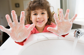 Girl at a sink showing off her soapy hands