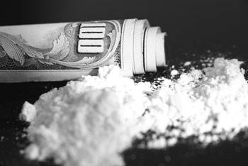 A pile of white powder next to a rolled-up hundred dollar bill