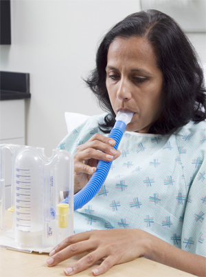 Woman in hospital gown breathing into spirometer tube.
