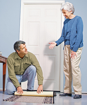 Younger man rolling up throw rug for older woman.
