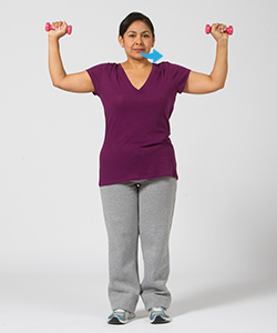 Woman breathing out while doing shoulder press exercise with hand weights.