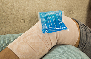 Closeup of elevated knee with bandage and ice pack.