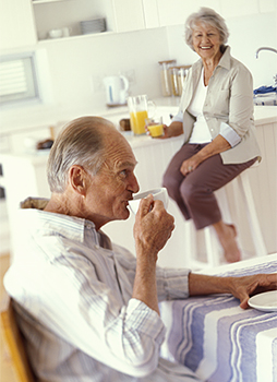 Senior man drinking tea. His wife is drinking orange juice and smiling at him.