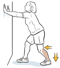 Woman leaning hands on wall doing gastrocsoleus calf stretch.
