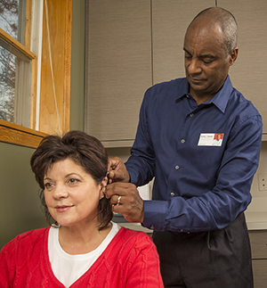 Healthcare provider fitting woman with hearing aid.