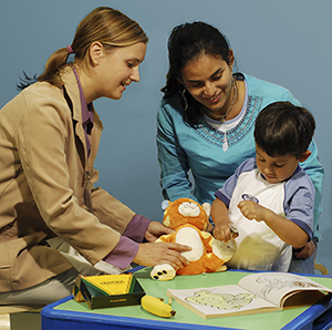 Healthcare provider and woman watching child play with medical toys.