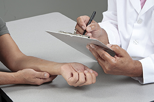 Healthcare provider writing on clipboard while patient rests arm on table.