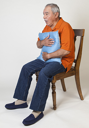 Man holding pillow to chest, coughing.