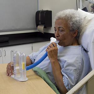 Woman wearing hospital gown using spirometer.