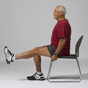 Man sitting in chair doing leg lift exercise.