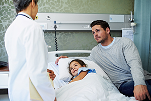 Girl in a hospital bed with her father talking to a doctor.