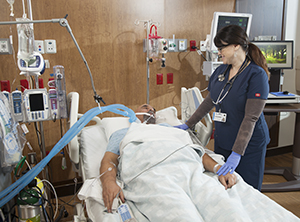 Healthcare provider caring for intubated man in intensive care unit bed.