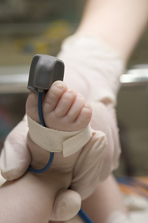 A baby's foot with a pulse oximetry sensor attached to a toe.