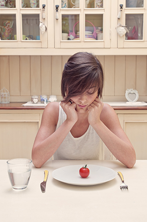 Young woman starting at small tomato on her plate.