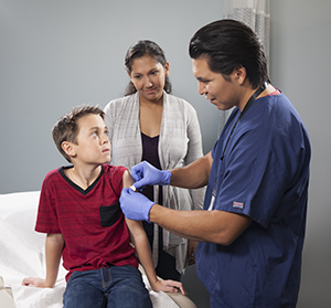 Healthcare provider giving boy injection in arm while woman looks on.