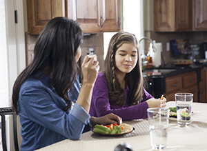 Woman bringing teen girl water and healthy snack in kitchen.