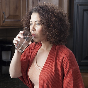 Woman drinking glass of water in kitchen.